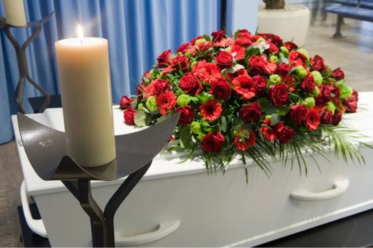 A coffin with a flower arrangement in a morgue and a burning candle in front